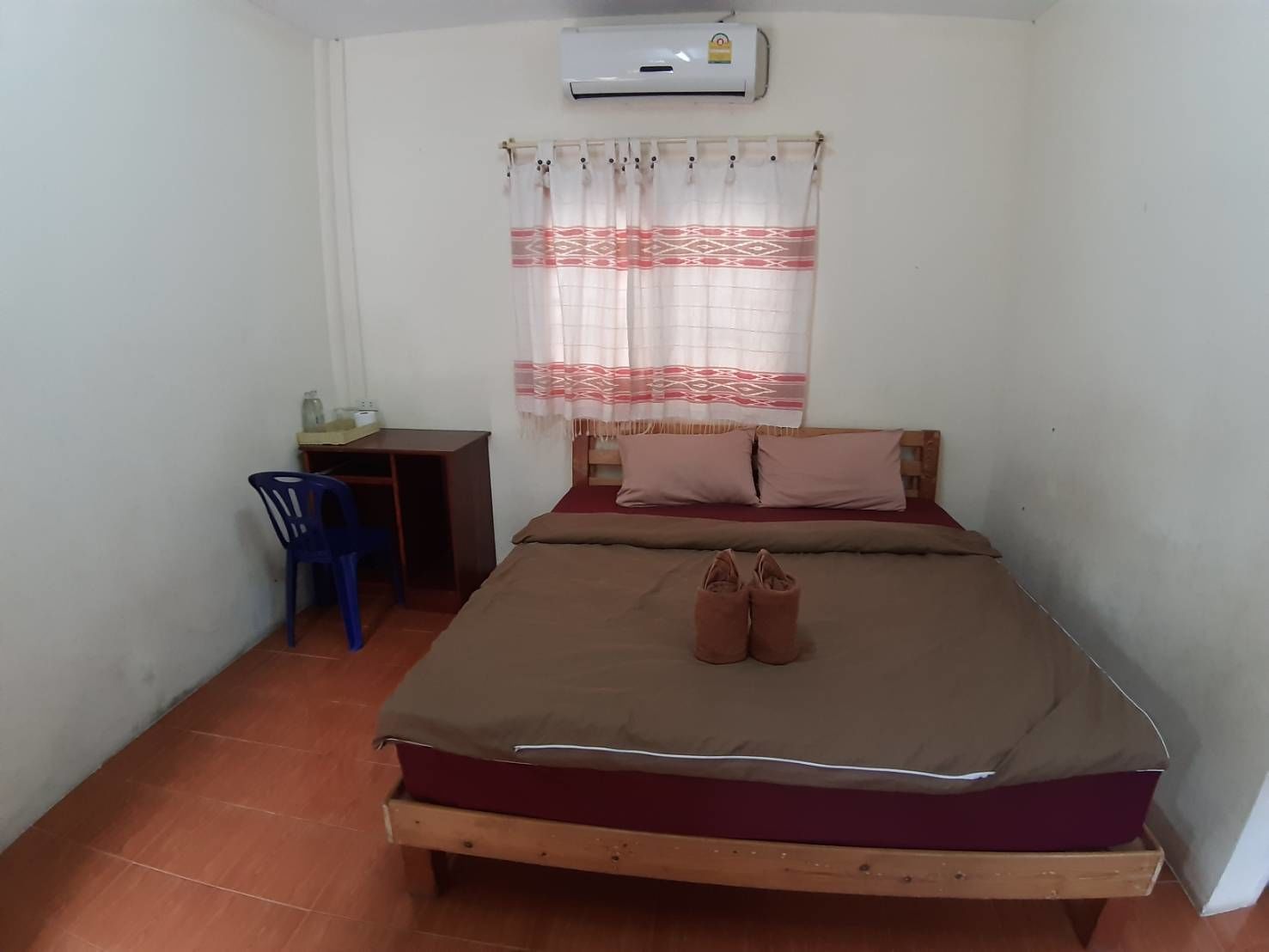 A small, simple room with a bed, a desk, a chair, and a window with a curtain.