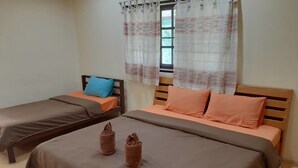 Quarto com duas camas de solteiro, cada uma com cabeceira de madeira, roupa de cama marrom e um travesseiro azul em uma das camas. Há toalhas nas camas e uma janela com cortinas estampadas.