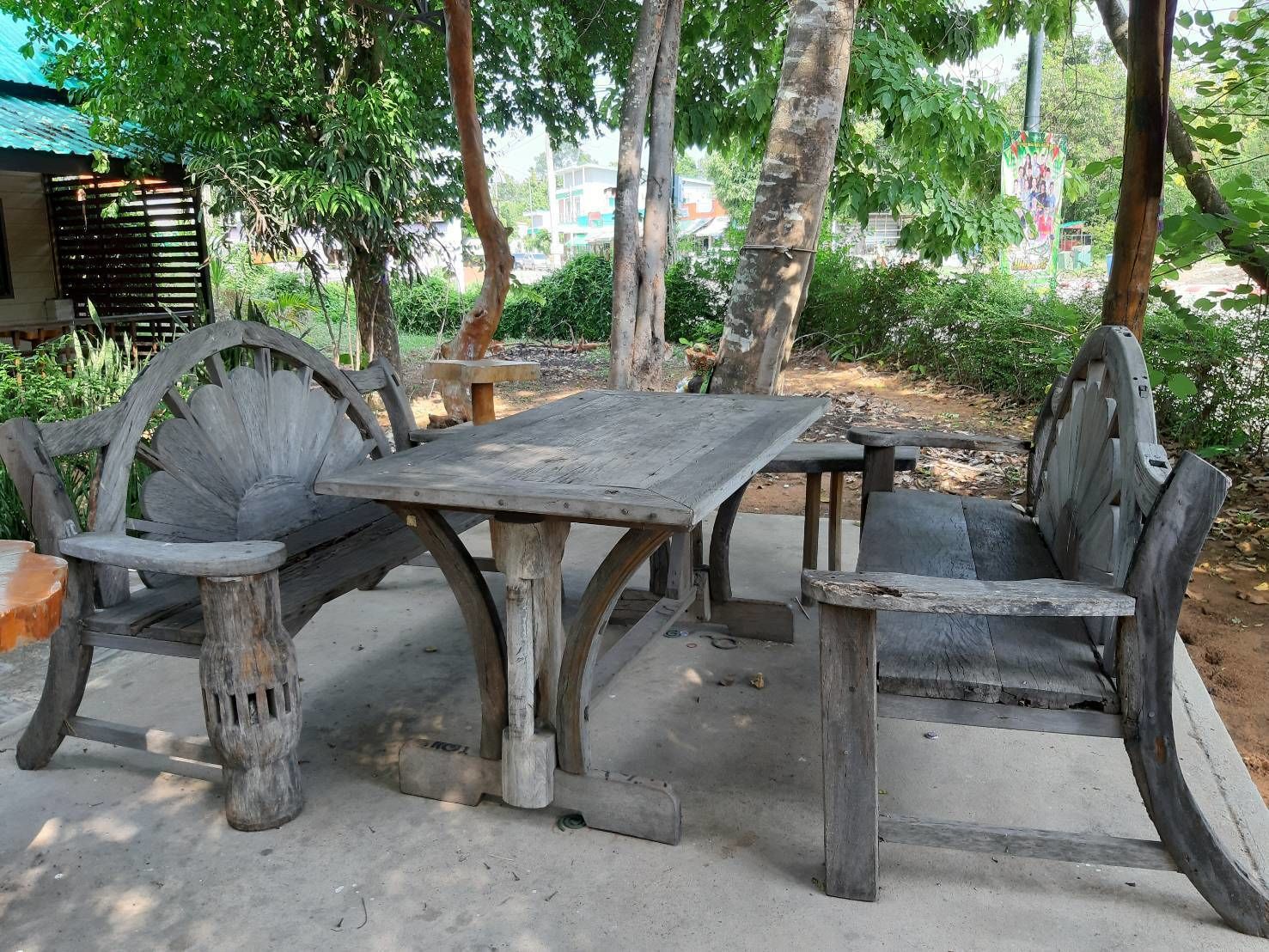 Un espace extérieur aménagé dans un style rustique, avec une table et des chaises en bois, entouré d’arbres et de verdure.