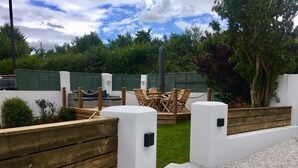 A patio area with wooden fences, a seating arrangement, and a white wall with a black mailbox. - Peaceful and comfortable HOUSE with COUNTRYSIDE views, 5 min drive to beach (Stratton, Bude)