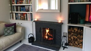 A cozy living room with a fireplace, a bookshelf, and a sofa. - Peaceful and comfortable HOUSE with COUNTRYSIDE views, 5 min drive to beach (Stratton, Bude)