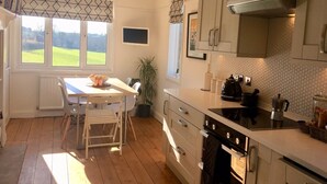 A kitchen with a dining area, wooden flooring, a stove, and a view of the outdoors. - Peaceful and comfortable HOUSE with COUNTRYSIDE views, 5 min drive to beach (Stratton, Bude)
