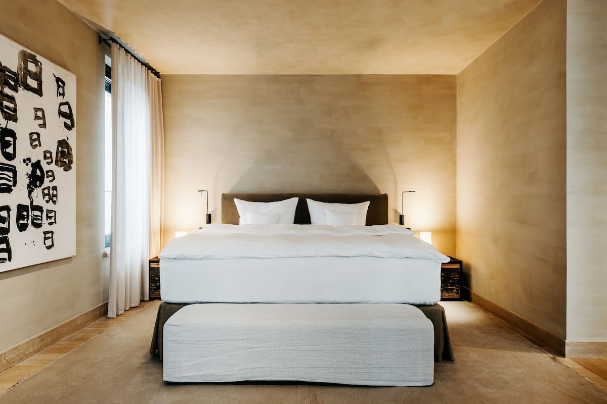 A modern bedroom with a large bed, a headboard, bedside tables, and a wall-mounted artwork.
