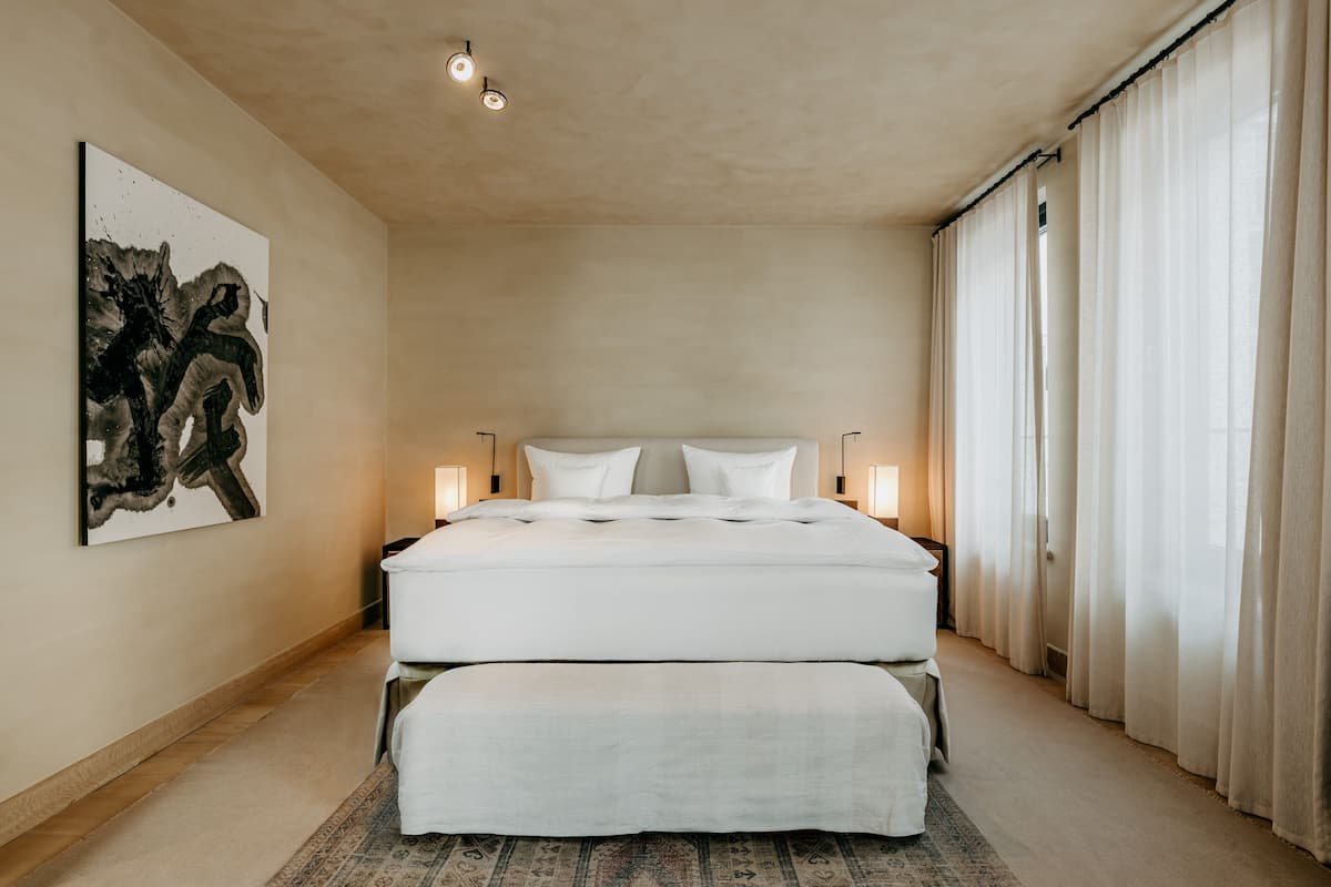 A spacious bedroom with a large bed, a bedside table, and a wall-mounted artwork.