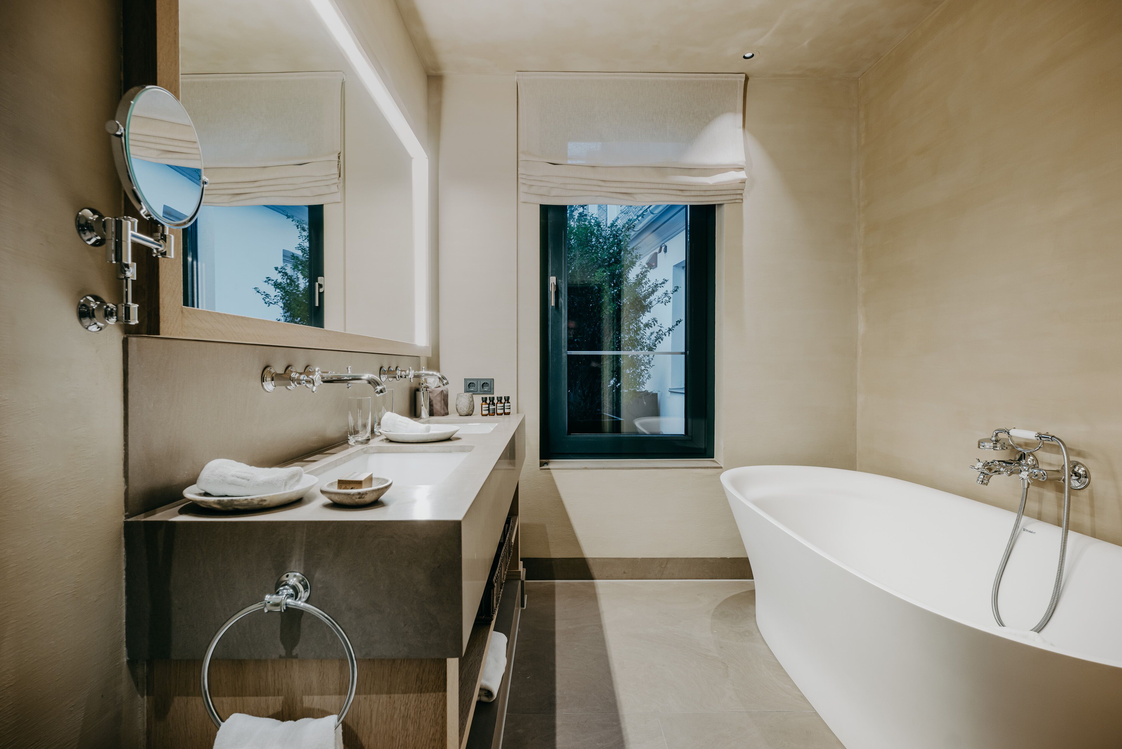 A modern bathroom with a freestanding bathtub, a double sink vanity, a large mirror, and a window providing natural light.