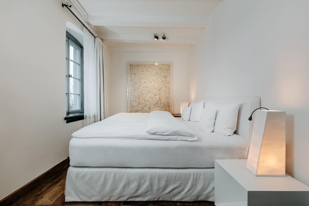 A modern bedroom with a large bed, a nightstand, and a wall-mounted light fixture.