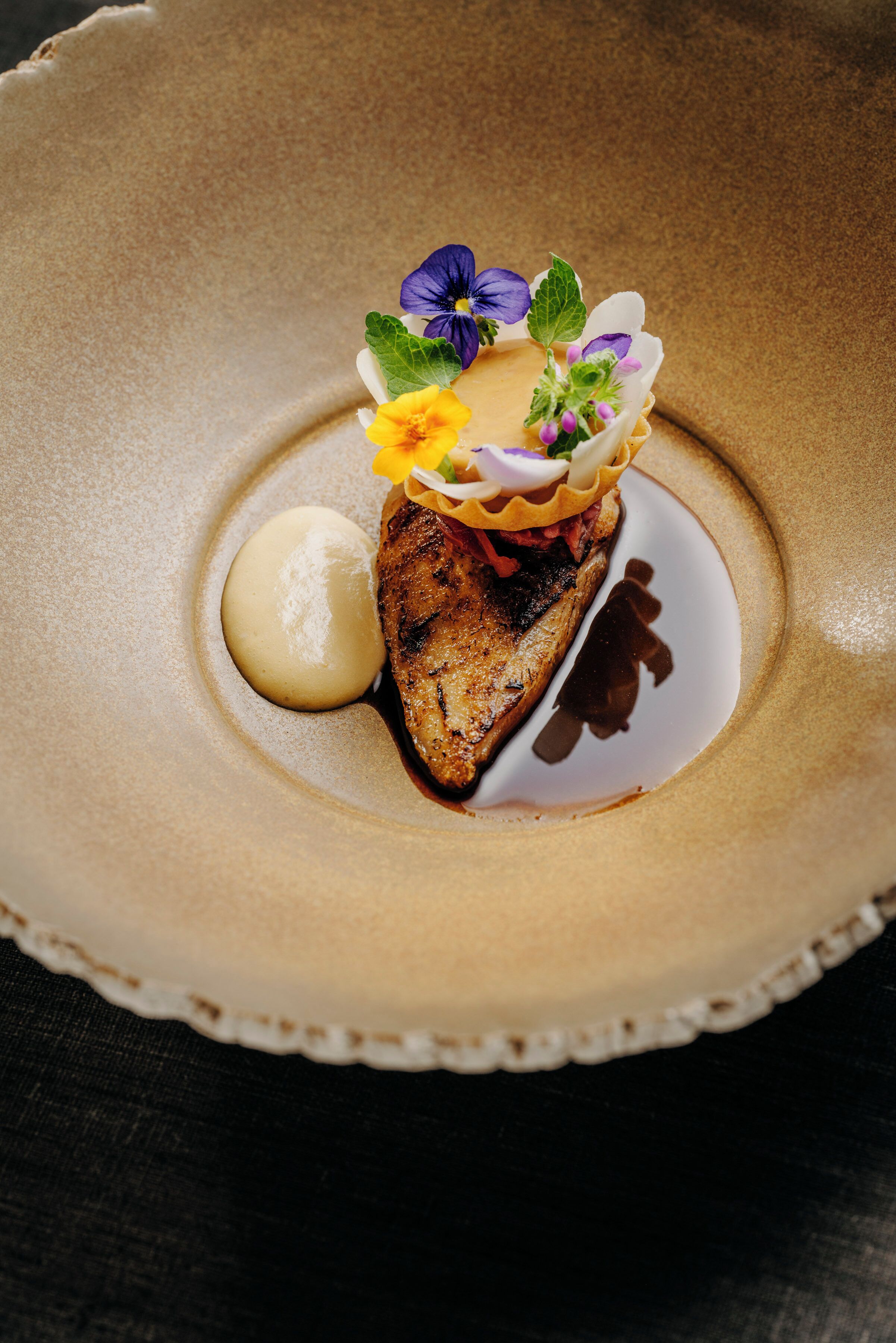 A dessert plate with a grilled meat centerpiece, garnished with flowers and a dollop of cream.