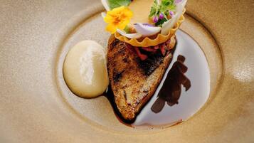 A dessert plate with a grilled meat centerpiece, garnished with flowers and a dollop of cream.