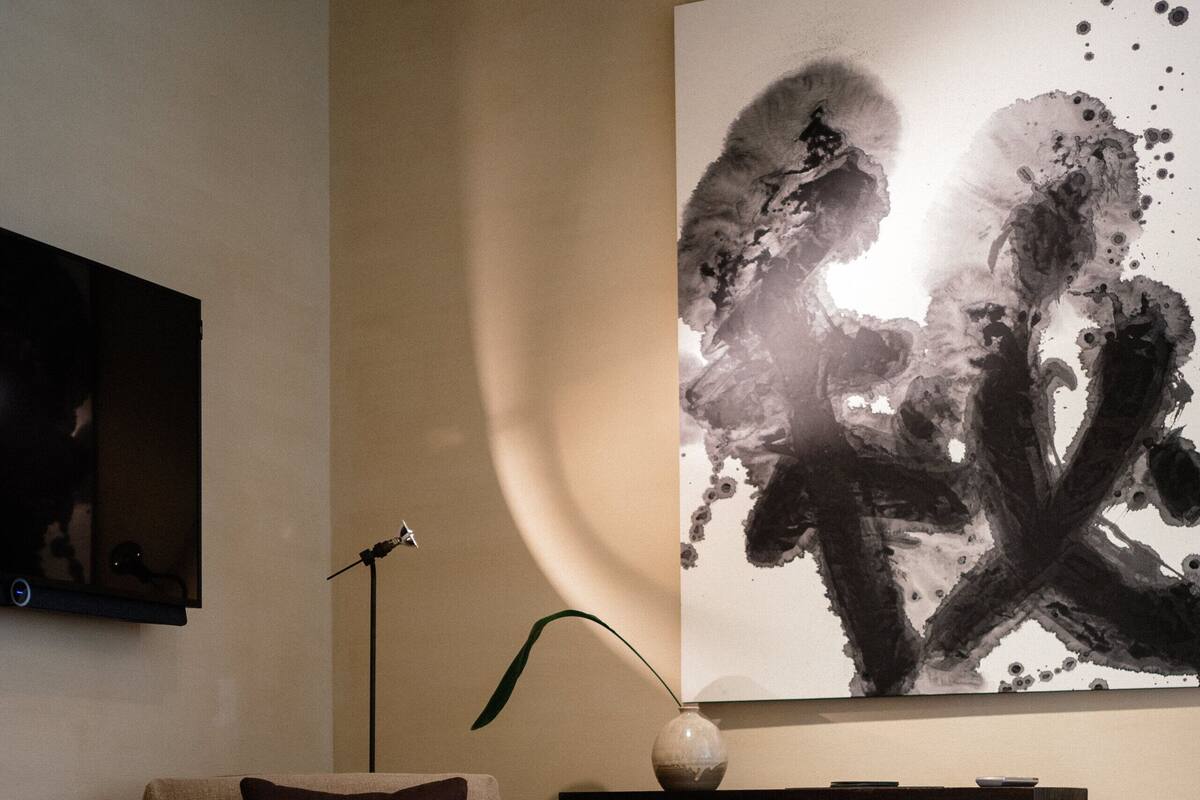 A modern living room with a beige armchair, a wooden cabinet, and a large abstract painting on the wall.