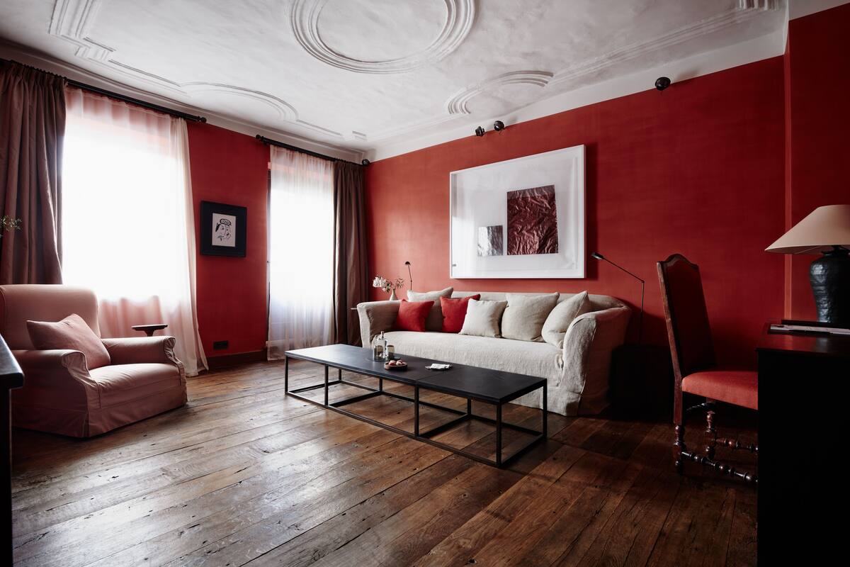 A living room with a red wall, a white ceiling, and a wooden floor. There is a sofa, a chair, and a coffee table.