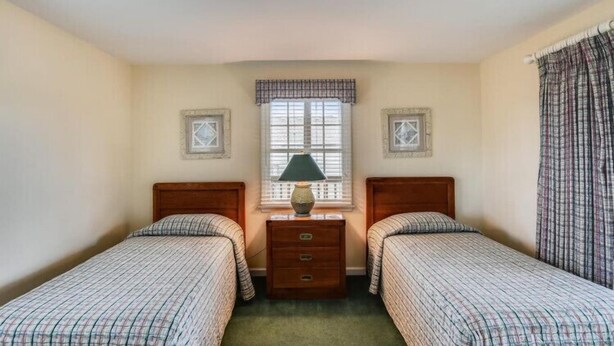 A room with two single beds, a nightstand with a lamp, a dresser, and a window with curtains. - The Myllet at Ships Watch in Duck (Duck)