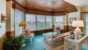 A room with a high ceiling, wicker furniture, and large windows with blinds. - The Myllet at Ships Watch in Duck (Duck)