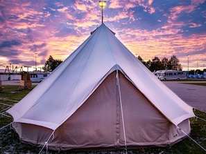 A large, white, pyramid-shaped tent with a central pole, set up on grass with a parking area in the background. - Festanation Oktoberfest Camp No.1 (Munich)