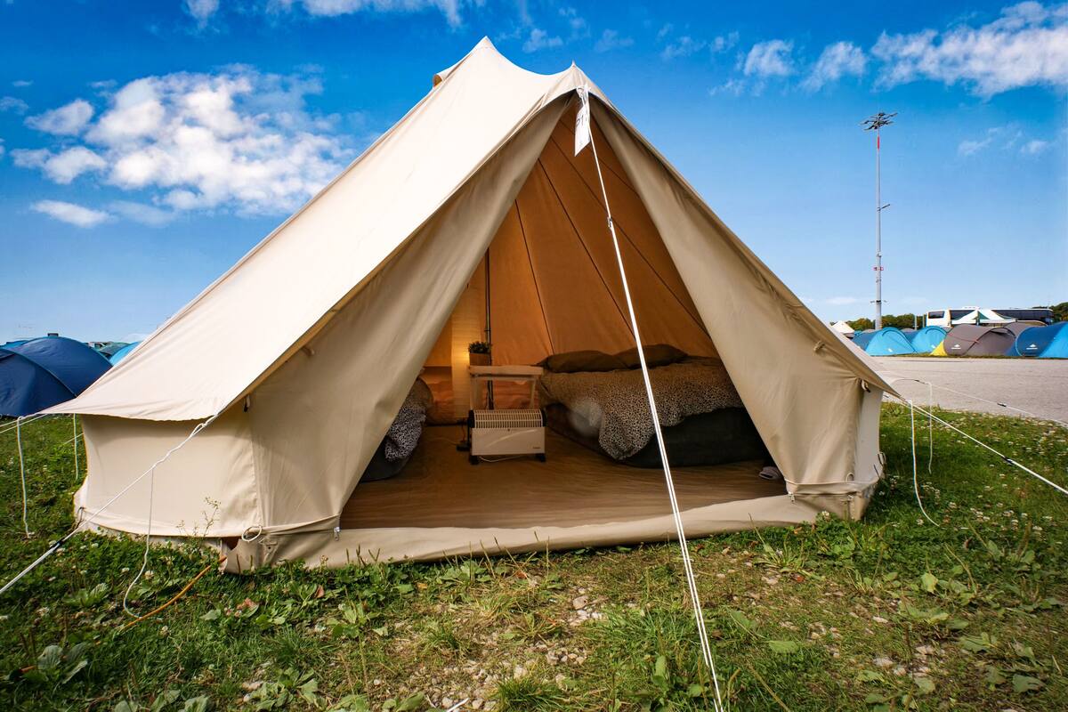 A dome-shaped tent with a bed inside, surrounded by grass and other tents.