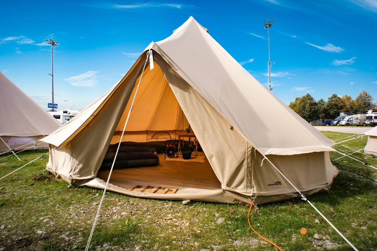 A large, beige, dome-shaped tent with a door, set up on a grassy field with other tents in the background.
