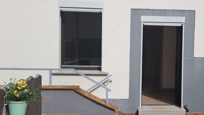 A building with a white exterior, a window, and a door. There is a small outdoor area with steps and a planter with yellow flowers. - Monteurwohnungen Viernheim (Viernheim)