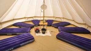A tent interior with multiple purple sleeping pads, a small table with a plant, and a hanging light fixture. - Festanation Oktoberfest Camp No.2 (Munich)