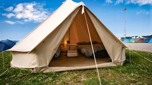 A dome-shaped tent with a bed inside, surrounded by grass and other tents. - Festanation Oktoberfest Camp No.2 (Munich)
