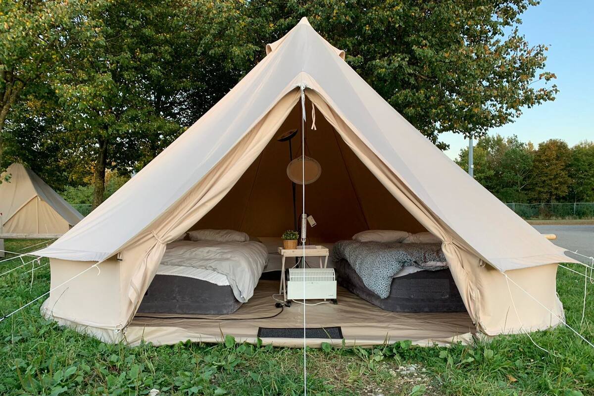 Een tent met twee bedden, een hanglamp en een klein tafeltje met een mand.