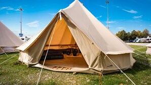 A large, beige, dome-shaped tent with a door, set up on a grassy field with other tents in the background. - Festanation Oktoberfest Camp No.2 (Munich)