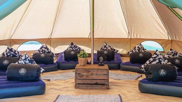 A large tent with a central wooden table, surrounded by purple sofas and patterned cushions. - Festanation Oktoberfest Camp No.2 (Munich)