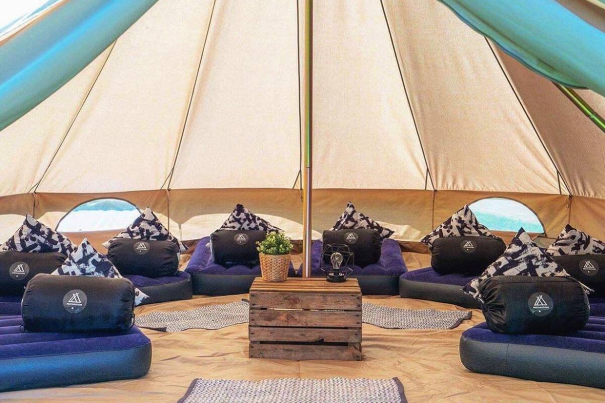 Een grote tent met een houten tafel in het midden, omringd door paarse banken en decoratieve kussens.