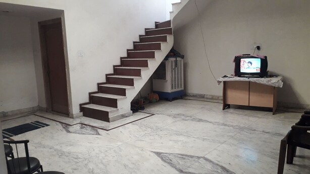 Una escalera que lleva a una plataforma, un televisor sobre un mueble bajo y un suelo de baldosas.