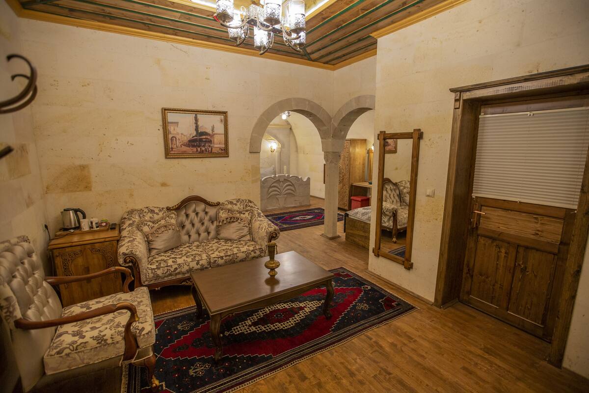 A room with a sofa, armchairs, a coffee table, a rug, a wooden cabinet, a mirror, and a door with a shutter.