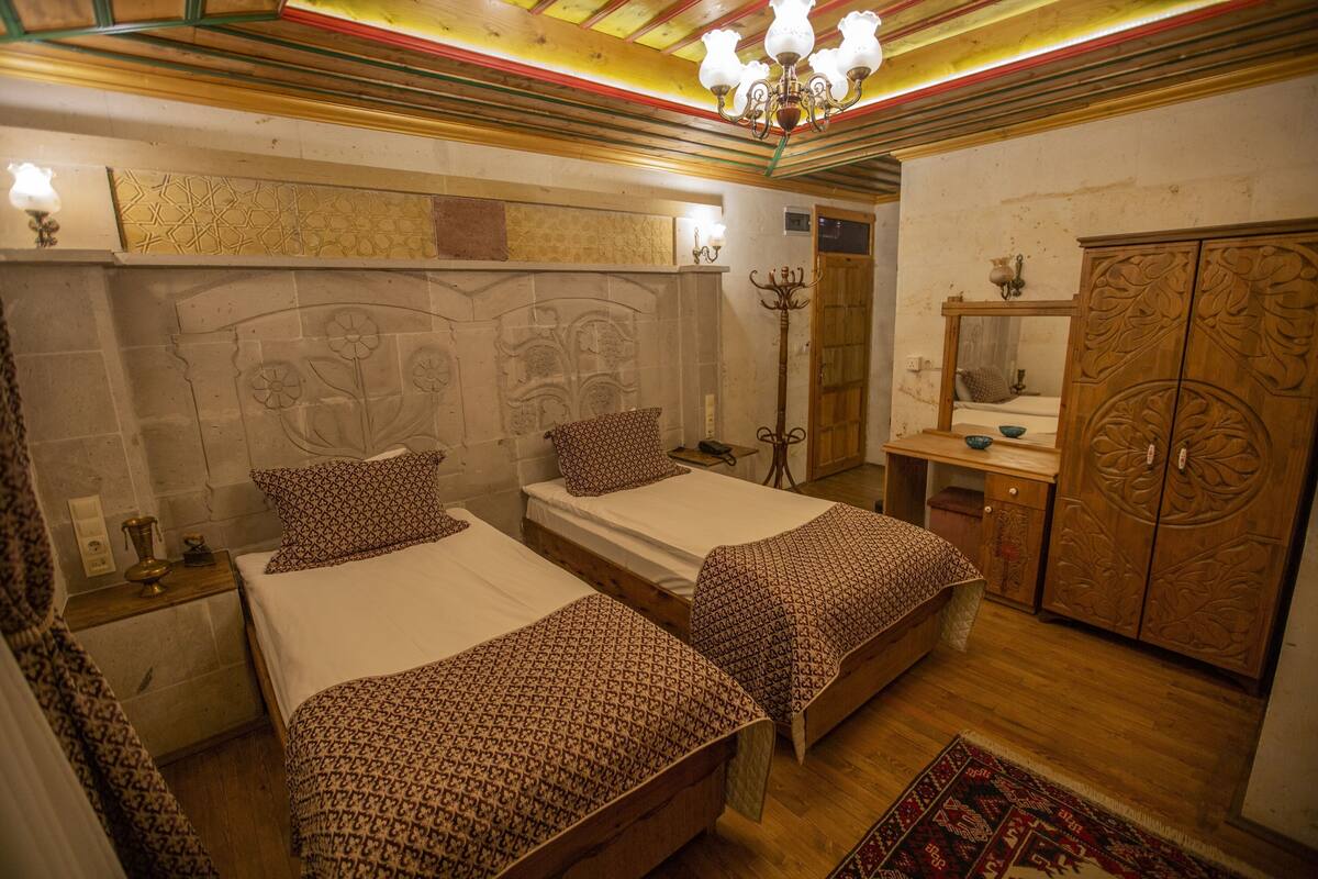 A room with two beds, a wooden wardrobe, a mirror, and a chandelier.