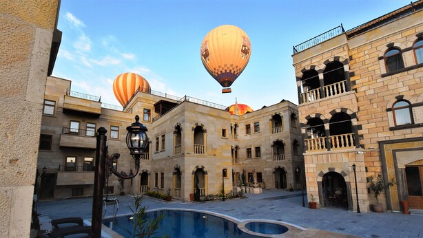A courtyard with a pool, hot air balloons, and historic buildings. - Goreme Reva Hotel (Nevsehir)