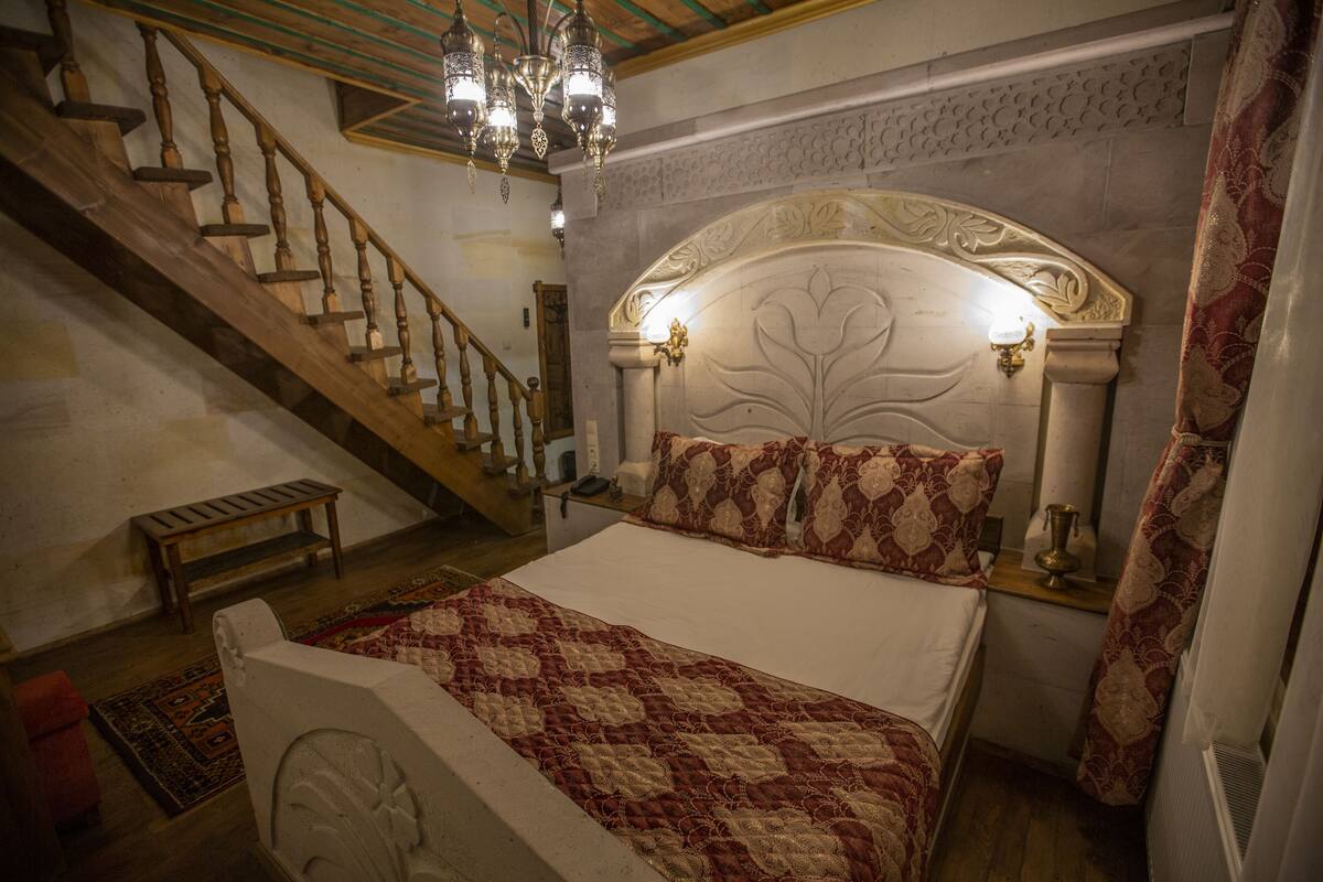 A bedroom with a large bed, a wooden staircase, and a chandelier.