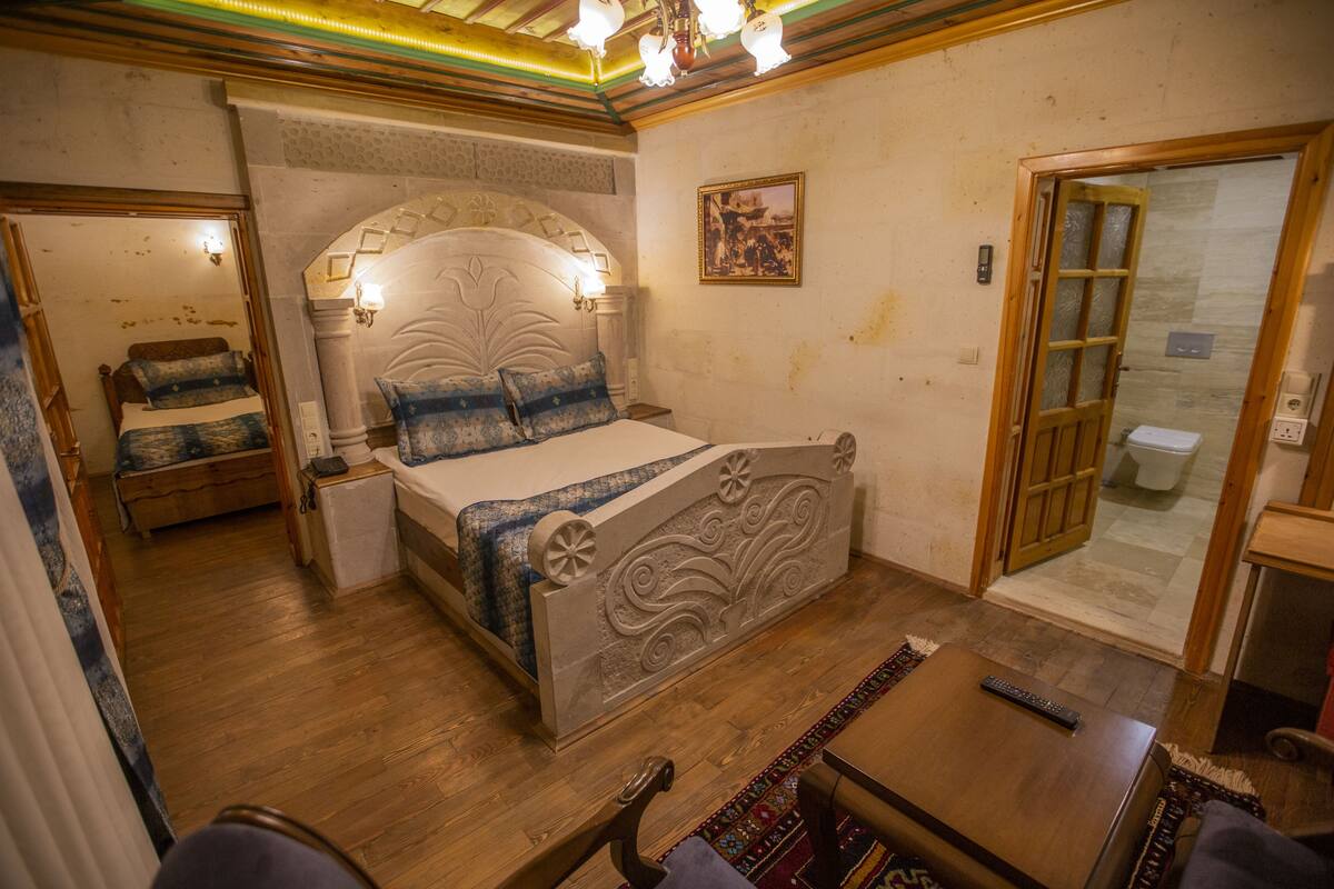 A bedroom with a large bed, a nightstand, a wooden table, and a bathroom visible through an open door.