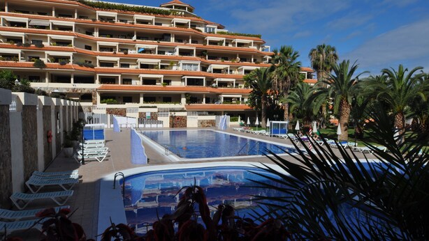 A hotel with multiple balconies, a swimming pool, and palm trees.