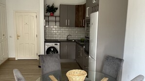 A modern kitchen with grey cabinets, a washing machine, and a glass dining table with grey upholstered chairs.