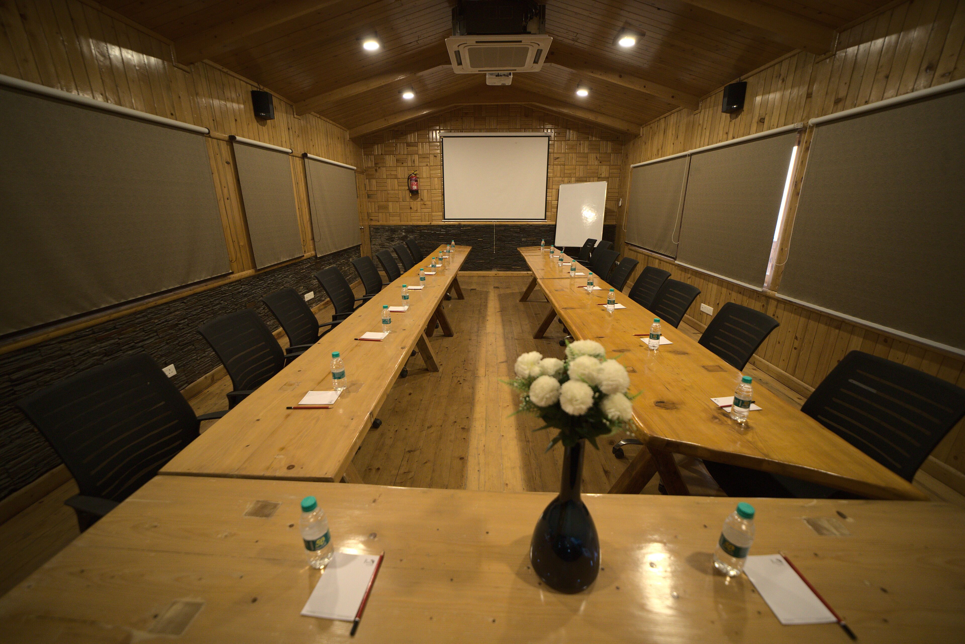 A conference room with a long table, chairs, a projector screen, and a whiteboard.