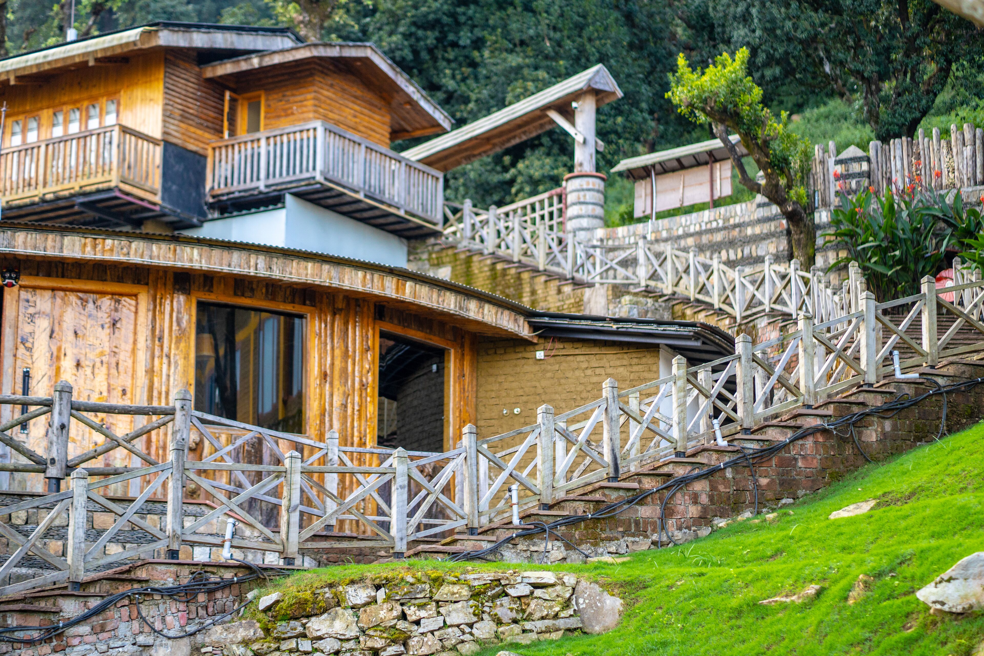 A wooden cabin with a balcony, a stone wall, and a wooden fence.