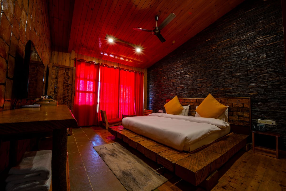 A bedroom with a wooden bed, red curtains, a ceiling fan, and a stone wall.