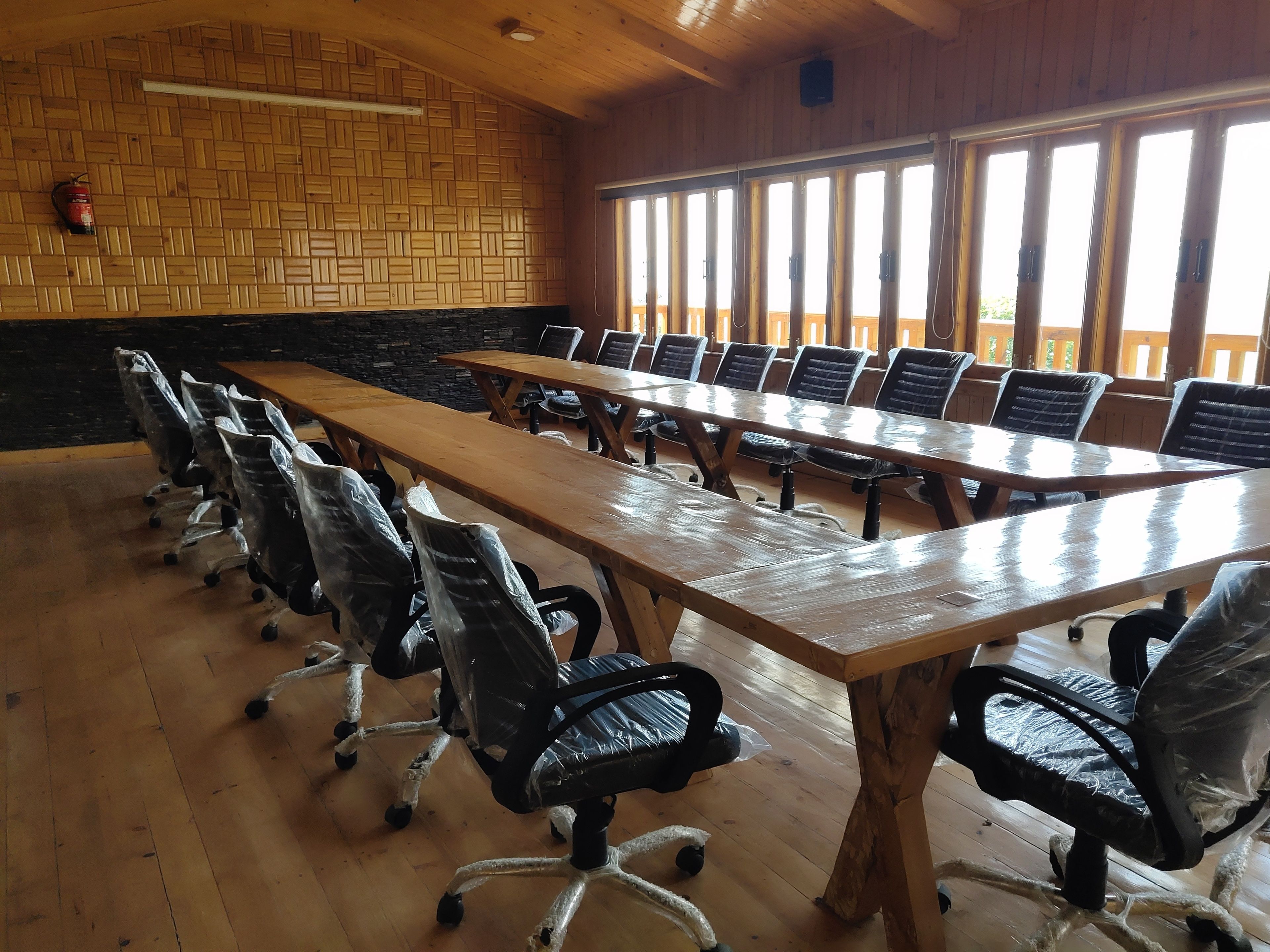 A conference room with long tables and chairs, wooden walls, and large windows.