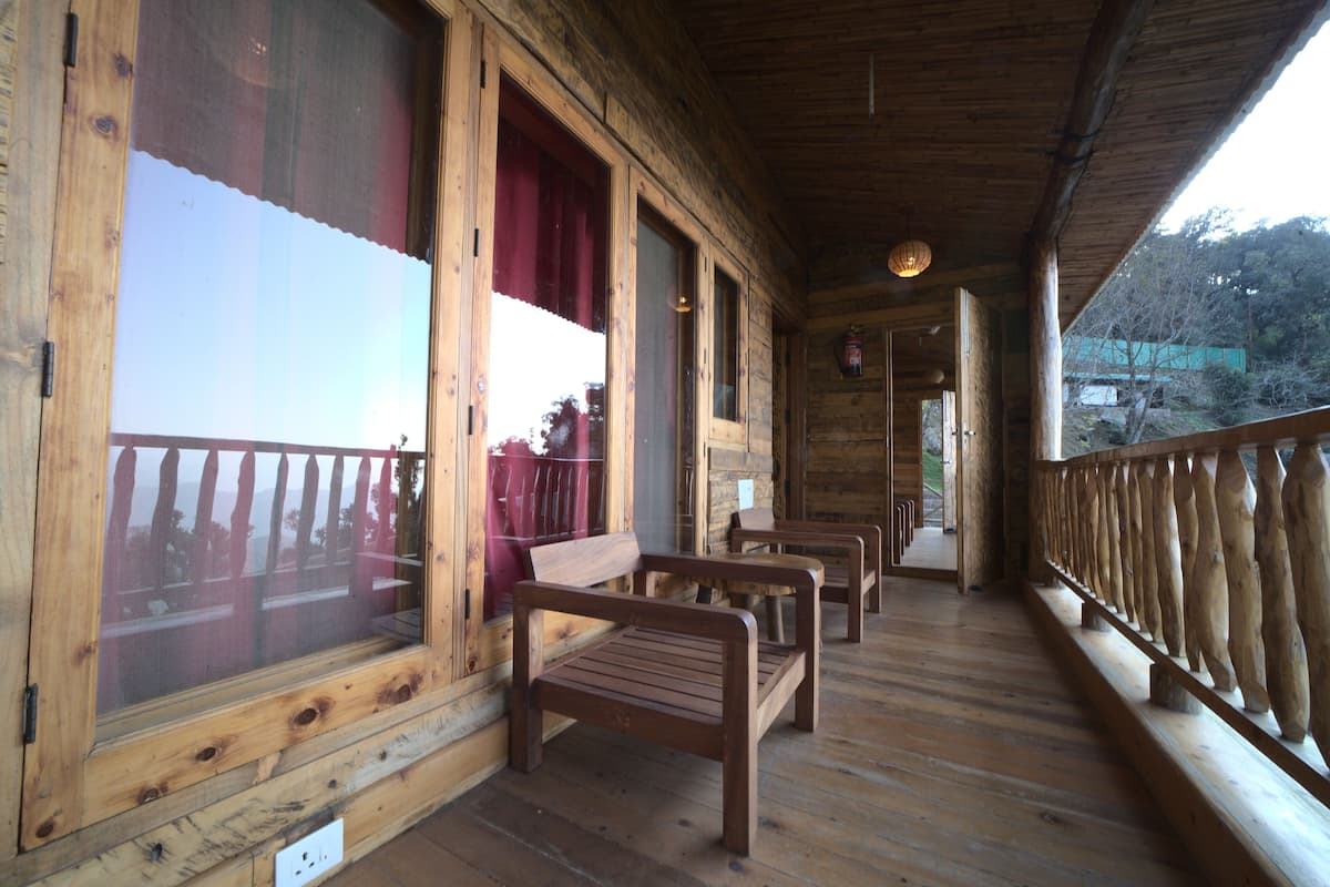 A wooden cabin with a porch featuring benches and a railing.
