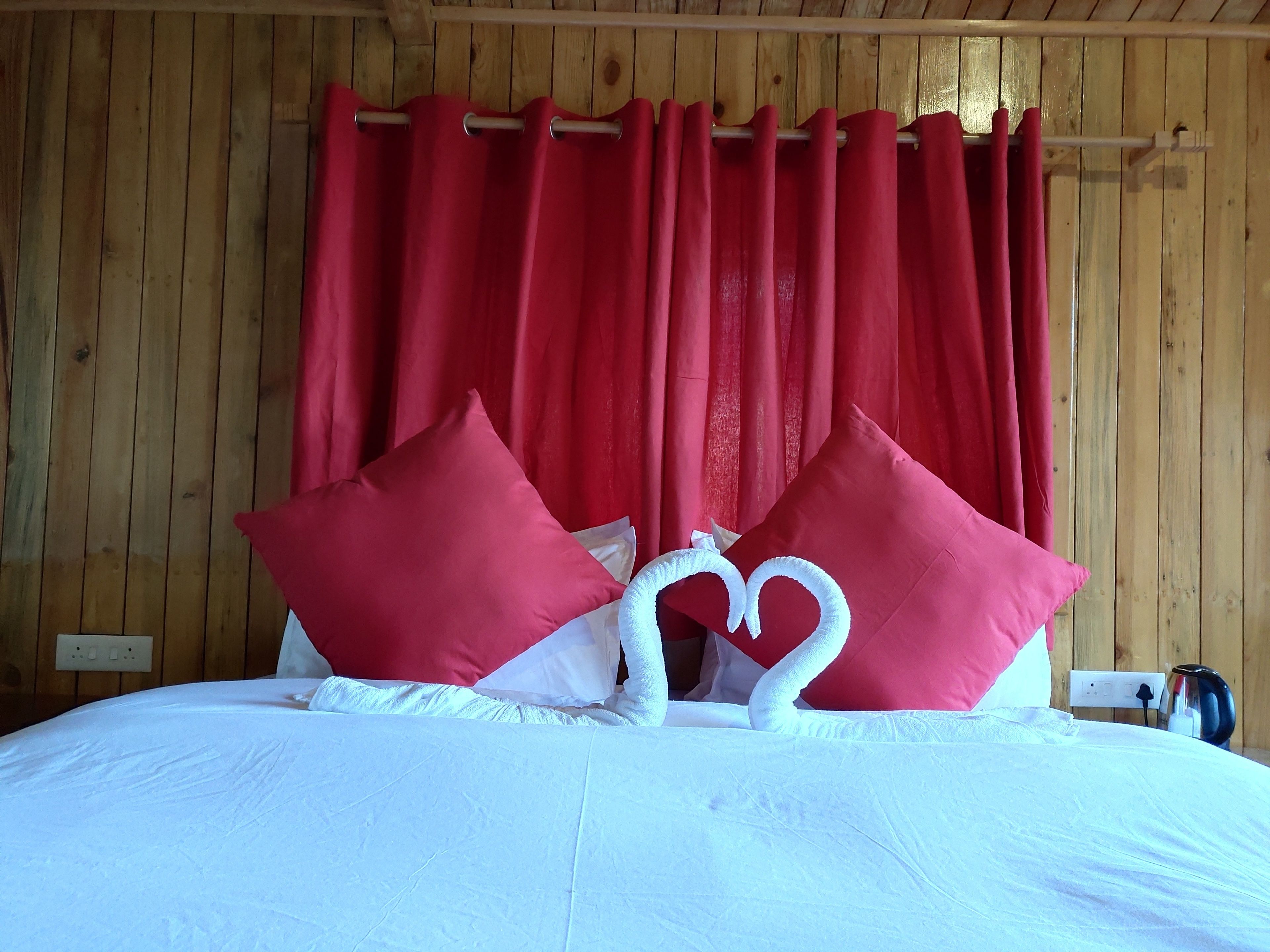 A bed with white bedding, red pillows, and a heart-shaped pillow arrangement.