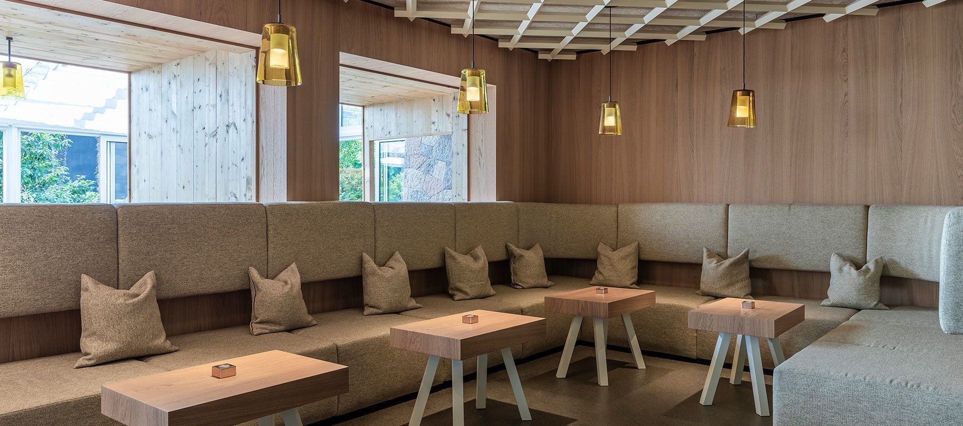 Ein modernes Interieur mit einer Holzvertäfelung, einer Sitzecke mit gepolsterten Bänken und Tischen sowie Pendelleuchten.