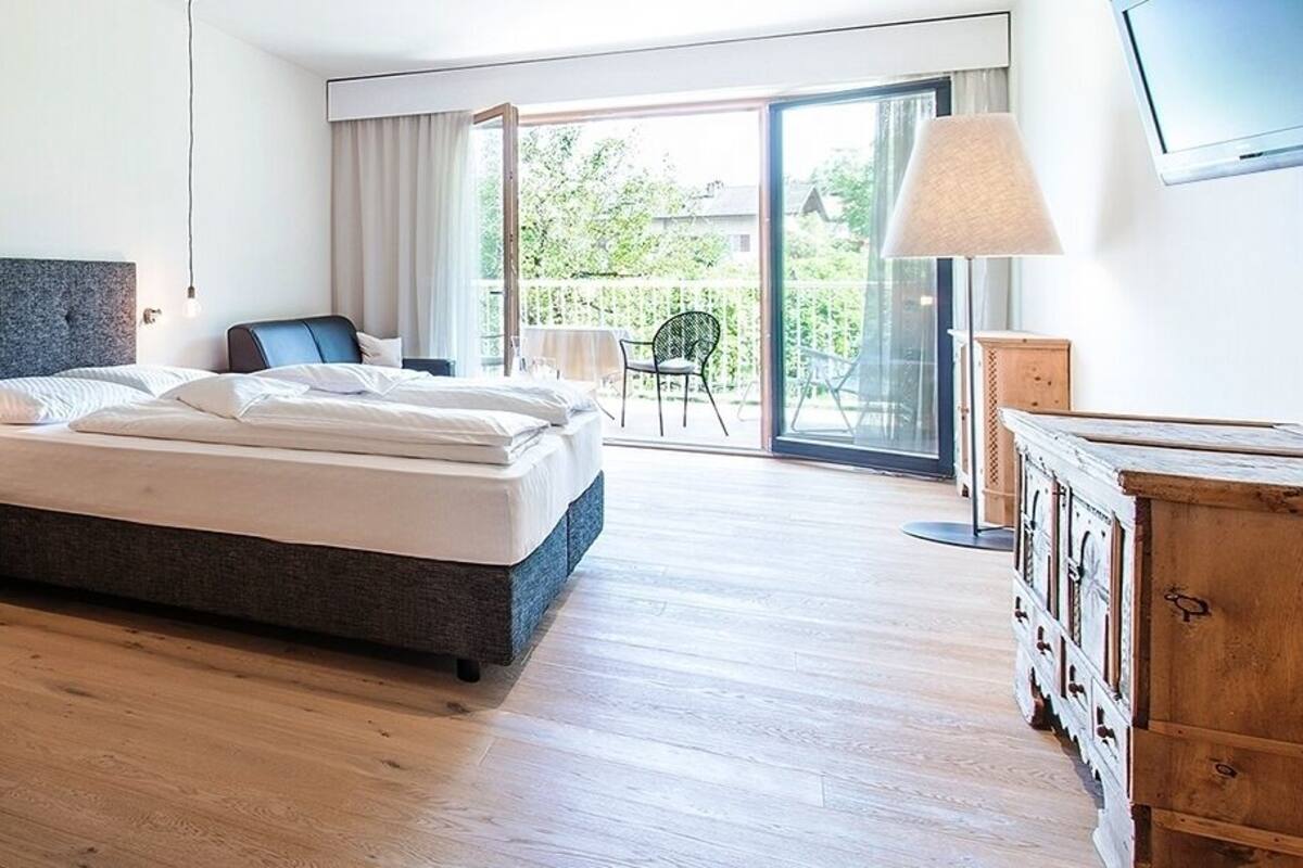 Une chambre à coucher avec un lit, une table à manger en bois avec des chaises, un saladier de fruits et une vue sur l’extérieur par une porte coulissante.