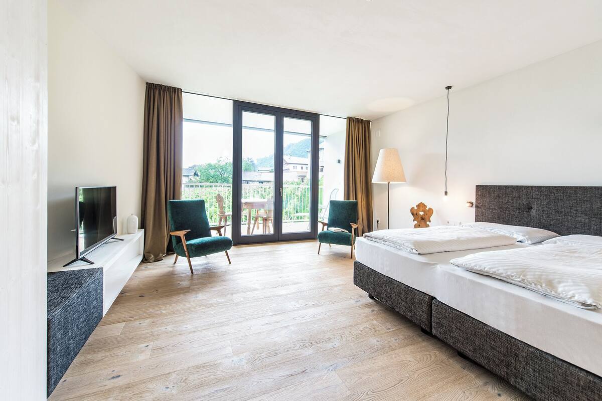 Une chambre d’hôtel avec un grand lit, deux fauteuils, une télévision et un balcon avec vue.