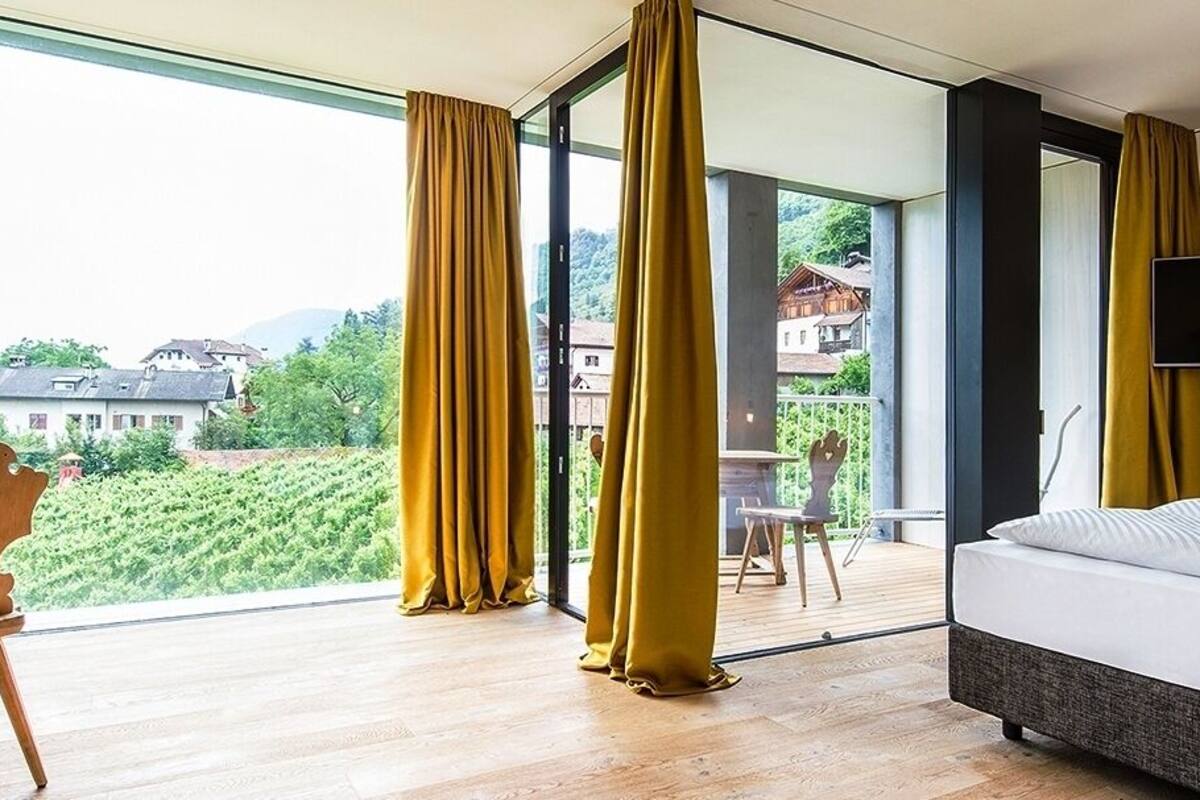 Une chambre d’hôtel comprenant un lit, un bureau avec une chaise, un téléviseur fixé au mur et une grande fenêtre donnant sur l’extérieur.