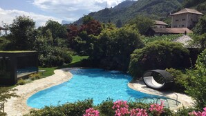A swimming pool with a stone pathway, surrounded by lush greenery and a hillside in the background. - Design-Hotel Ballguthof (Lana)