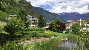 A residential area with a pond, lush greenery, and mountains in the background. - Design-Hotel Ballguthof (Lana)