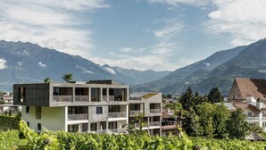 A modern building with a balcony, surrounded by vineyards and mountains in the background. - Design-Hotel Ballguthof (Lana)