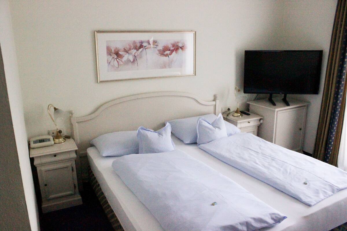 Une chambre d’hôtel avec un lit, une table de chevet avec une lampe, une télévision et un tableau encadré au mur.