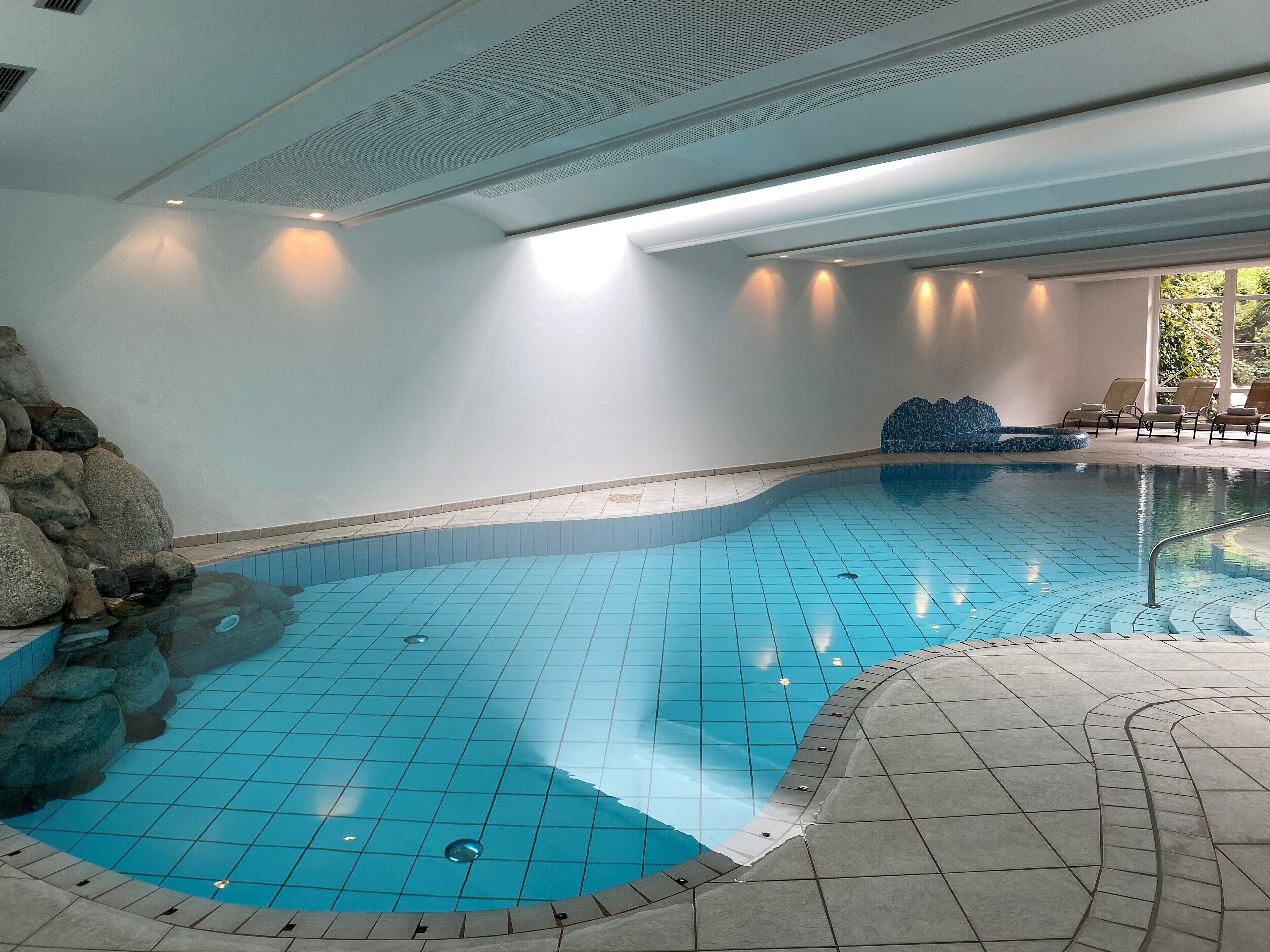 A swimming pool with tiled flooring and a stone wall on one side.