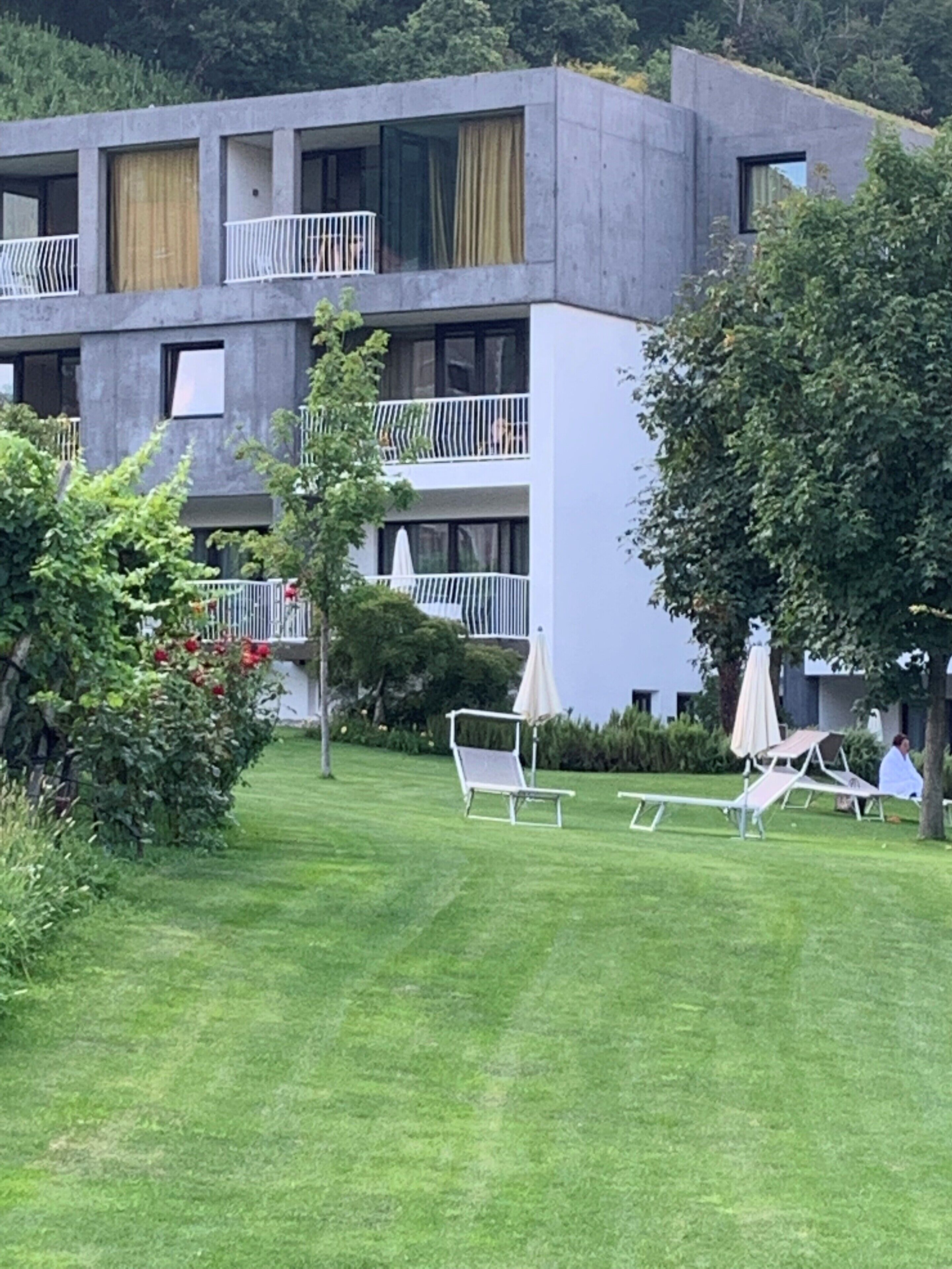A modern building with a flat roof, multiple balconies, and a well-maintained lawn with outdoor seating.